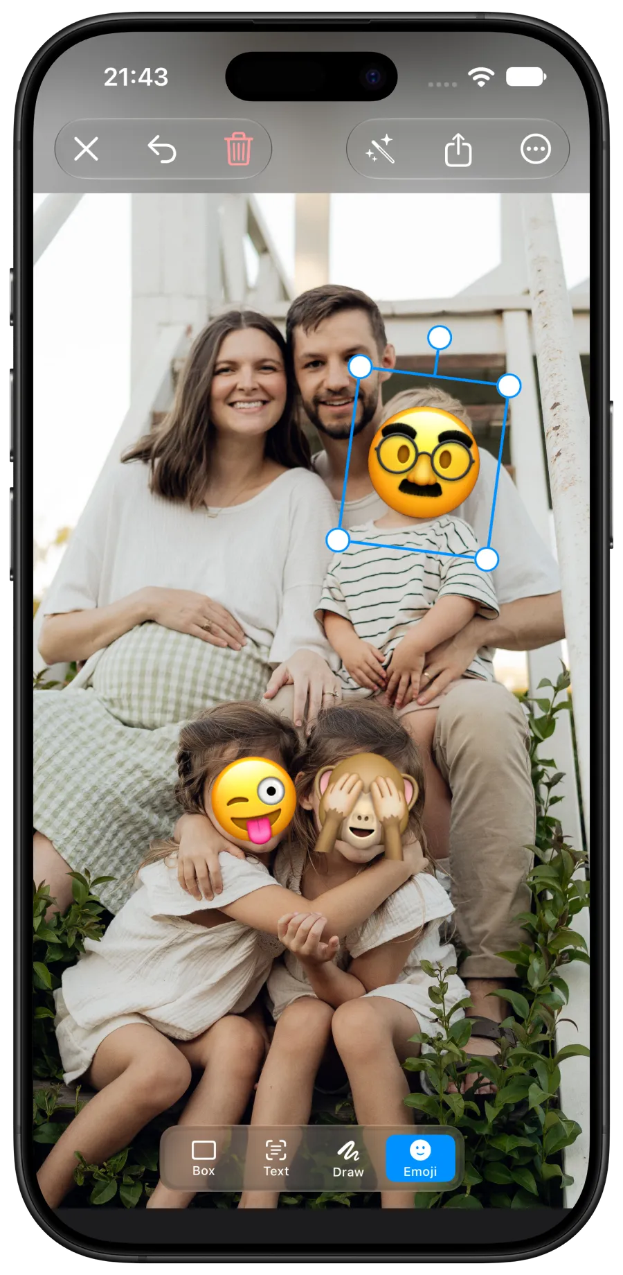 The Redacted iPhone app covering three faces in a family photo with emoji, one mask still selected for resizing.
